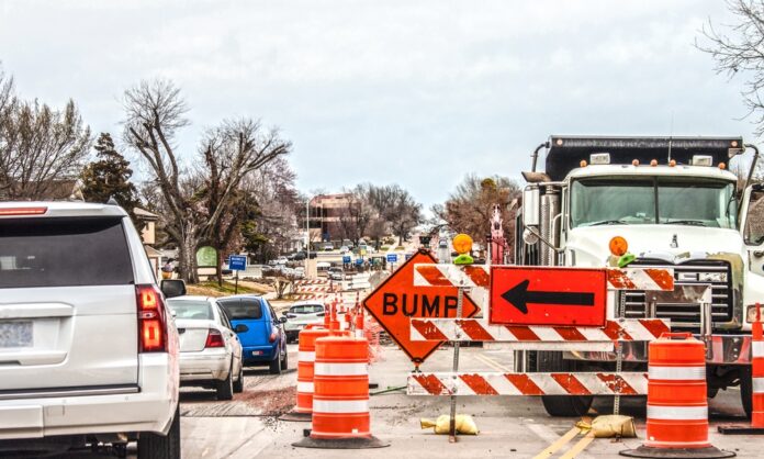 A road with heavy construction underway. Safety cones line the middle of a street with a sign saying "bump."
