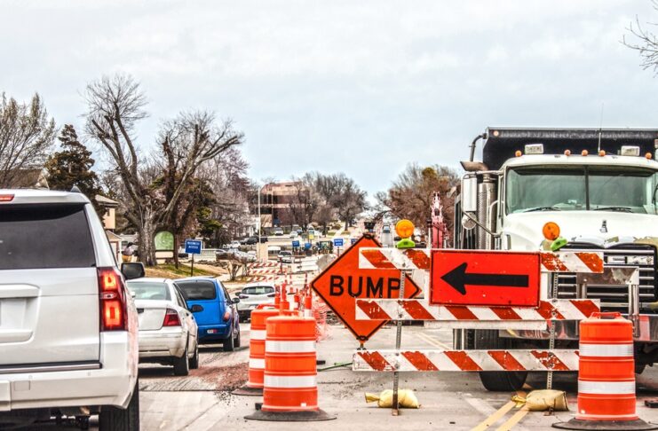 A road with heavy construction underway. Safety cones line the middle of a street with a sign saying "bump."