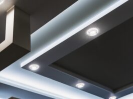 A dark-colored recessed ceiling features industrial beams and several circular LED lights that are turned on.