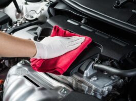 A close-up of a person wearing a glove while using a red cloth to clean the engine area of a vehicle.