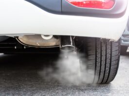 A closeup on the exhaust system of a white car. There is a plume of white smoke coming out of the tailpipe.