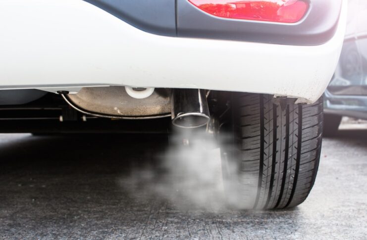 A closeup on the exhaust system of a white car. There is a plume of white smoke coming out of the tailpipe.