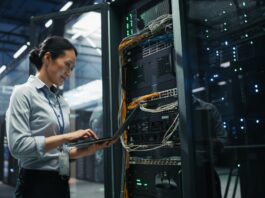 Liquid Cooling Is Becoming Standard for AI Servers A woman using a laptop beside an open server rack with cables and glowing equipment in a large data center.