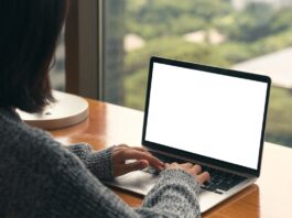 Beginner Tips for Getting More From Your MacBook An over-the-shoulder view shows a woman sitting at a desk typing on a laptop keyboard. The desk faces a large window.