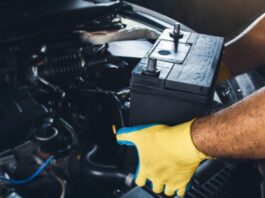 The Importance of Routine Car Battery Maintenance A mechanic wearing yellow-and-green gloves to remove a large black battery from a car in a repair shop.