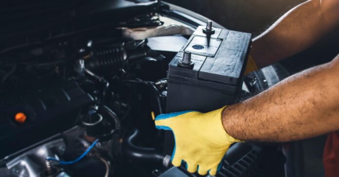 connector-experts-458629-gloves-battery-car-image1 A mechanic wearing yellow-and-green gloves to remove a large black battery from a car in a repair shop.